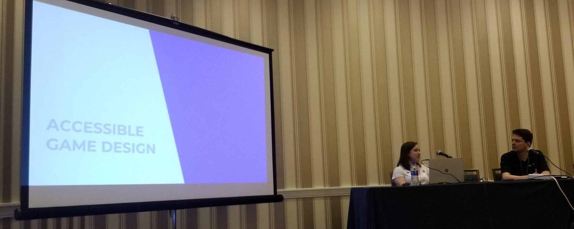 Ruthie Edwards and Daniel Greenberg on a conference center stage near a slideshow that says Accessible Game Design
